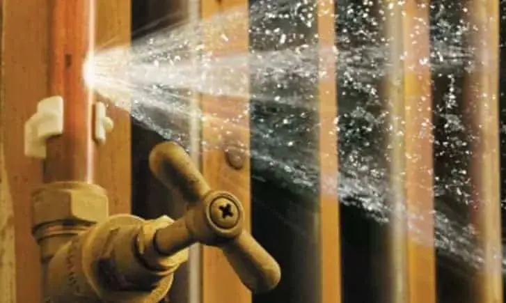 Water spraying from a burst supply pipe at a shutoff valve inside a wall